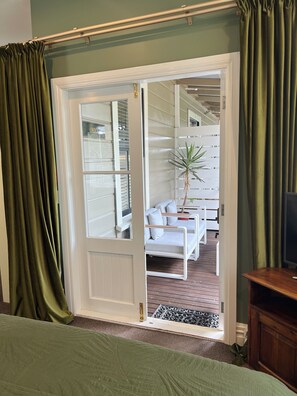 A room with a sliding door leading to an outdoor seating area, a bed with a green bedspread, and a wooden nightstand.