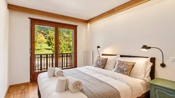 Une chambre avec un grand lit, une vue sur la verdure grâce à une porte coulissante, et une table de chevet avec une lampe.