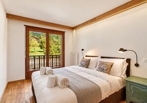 Une chambre avec un grand lit, une vue sur la verdure grâce à une porte coulissante, et une table de chevet avec une lampe.