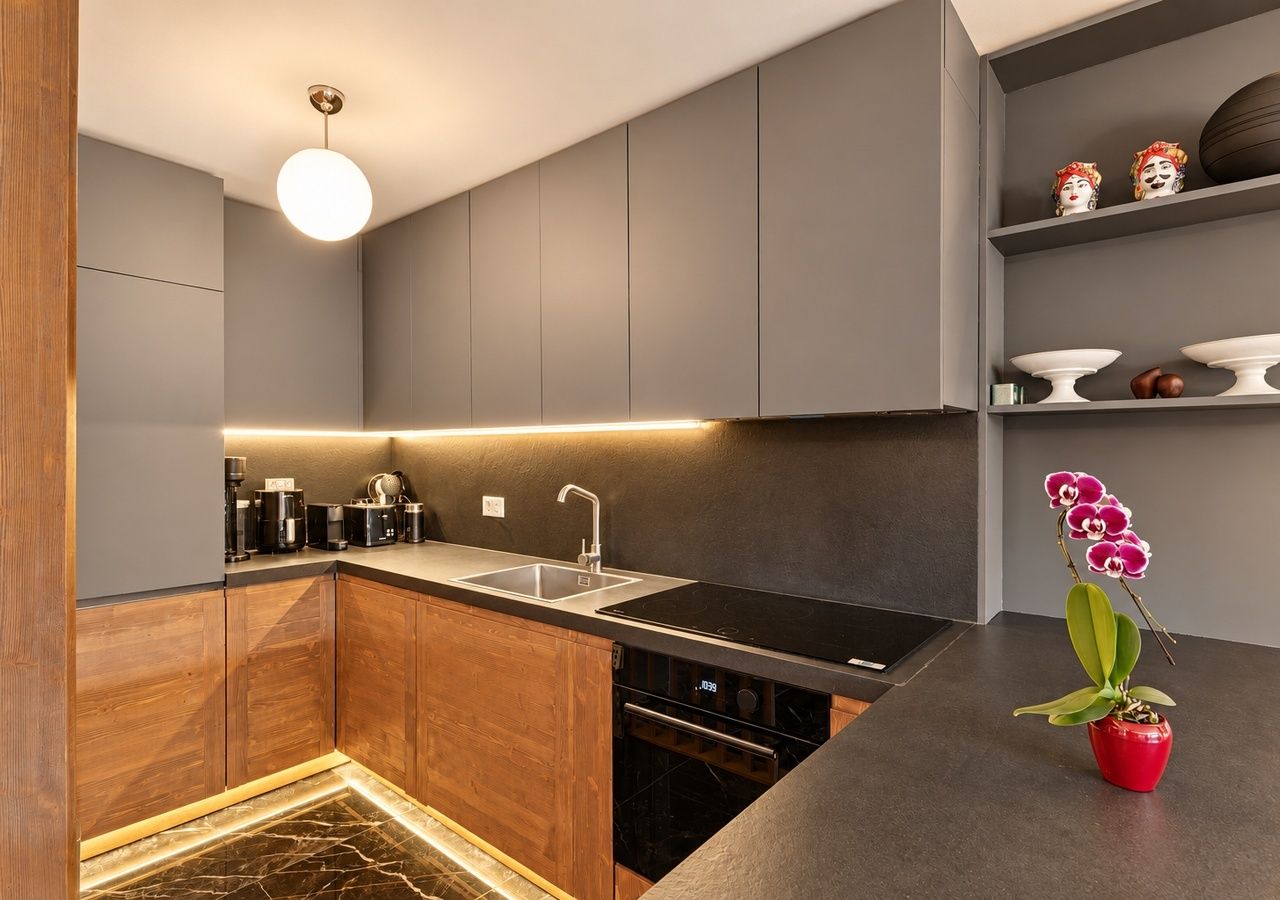 A modern kitchen with grey cabinetry, a black countertop, and a single pendant light.