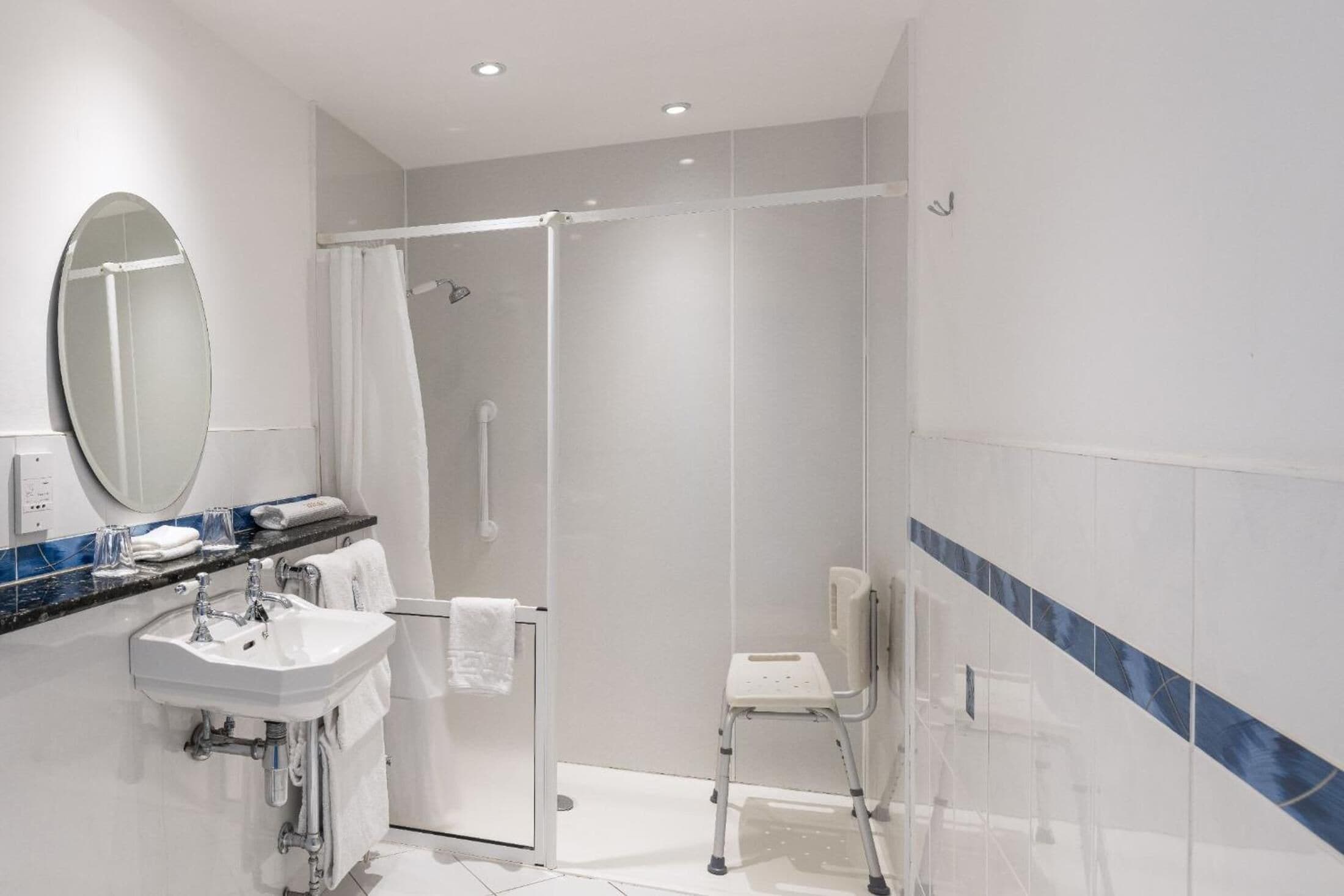 A modern bathroom with a glass shower enclosure, a white sink, a mirror, and a white chair.