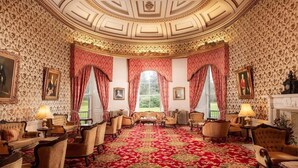 Una sala formal con alfombra estampada, techo ornamentado y muebles clásicos.