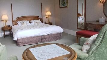 Quarto de hotel com uma cama grande, luminárias laterais, uma mesa redonda, uma poltrona verde e um espelho.