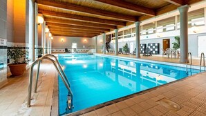 Una piscina interior con techo de madera, suelo de baldosas y un letrero que indica la zona de aguas profundas.