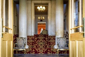 En imponerende trappe med detaljeret tæppe og søjler, der fører op til et rum med en lysekrone.