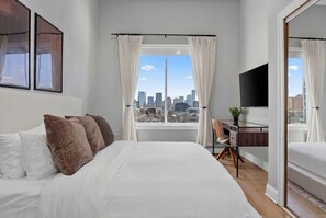 A bedroom with a bed, a desk, a chair, a TV, and a city view. - NYC View Patio, Fire Pit, Sleeps 8 (North Bergen)