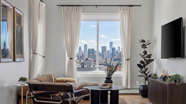 Una sala de estar moderna con vista a la ciudad, un sofá, una mesa de centro, un televisor y una planta en maceta.