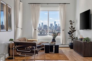 Ein modernes Wohnzimmer mit Stadtblick, einer Couch, einem Couchtisch, einem Fernseher und einer Topfpflanze.