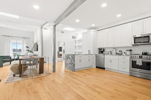 A modern kitchen with white cabinets, a marble island, stainless steel appliances, and a dining area with a wooden table and chairs. - NYC View Patio, Fire Pit, Sleeps 8 (North Bergen)