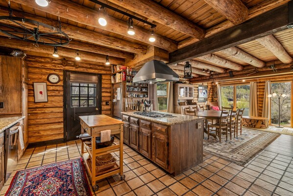 A rustic cabin interior with a kitchen, dining area, and large windows.