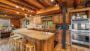 A log cabin interior with a large kitchen island, wooden bar stools, and a stone countertop.