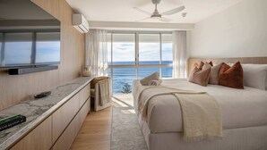 Una camera da letto con un letto, una TV, una ventola a soffitto e vista sull'oceano.