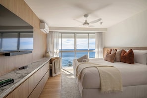 A bedroom with a bed, a TV, a ceiling fan, and a view of the ocean. - Ember by Khove (Burleigh Heads)