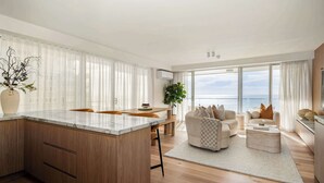Un soggiorno moderno con isola cucina, zona pranzo e posti a sedere vicino a una grande finestra con vista sul mare.