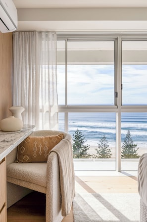 A room with a large window, a sofa with a blanket, a marble table, and a decorative vase. - Ember by Khove (Burleigh Heads)
