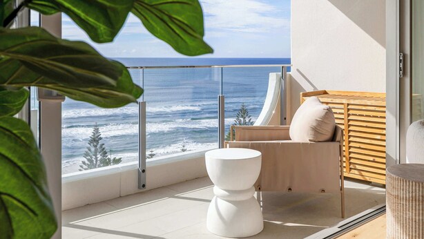 Un balcone con vista sull'oceano, un water bianco e una panca di legno.