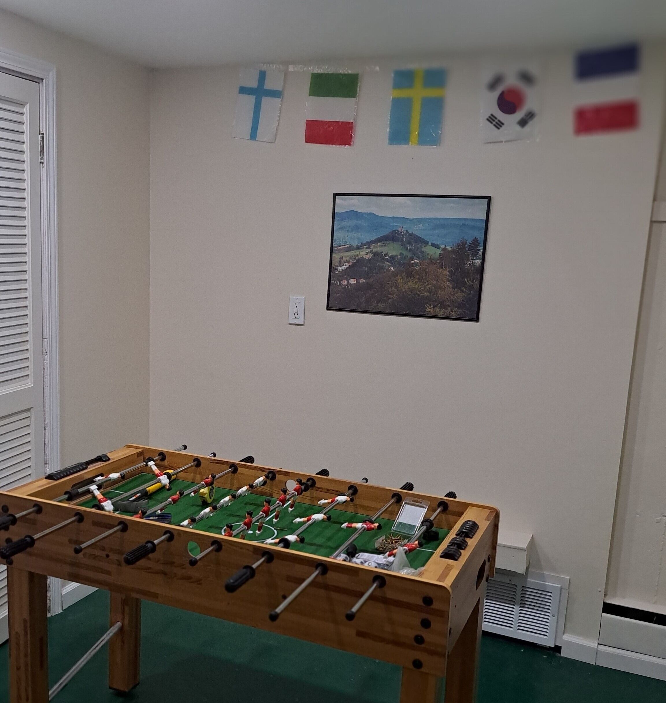 A room with a foosball table, a wall-mounted painting, and flags.