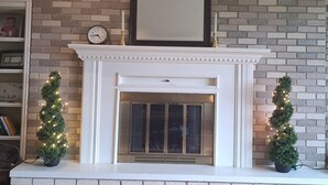 A fireplace with a white mantel, a clock, and two small potted Christmas trees with lights. - Creekside Retreat at Notre Dame (South Bend)