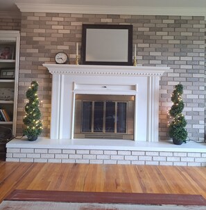 A fireplace with a white mantel, a clock, and two small potted Christmas trees with lights.