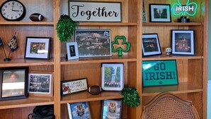 A room with a wooden shelf displaying various framed photos, a clock, and a neon sign. - Creekside Retreat at Notre Dame (South Bend)