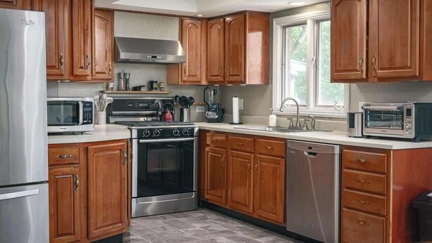 A modern kitchen with wooden cabinets, stainless steel appliances, and a large window providing natural light. - Creekside Retreat at Notre Dame (South Bend)