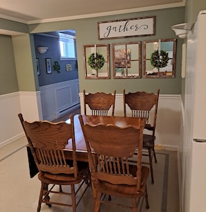 A dining area with a wooden table and chairs, a wall-mounted sign that says 'gathers,' and framed mirrors with greenery.