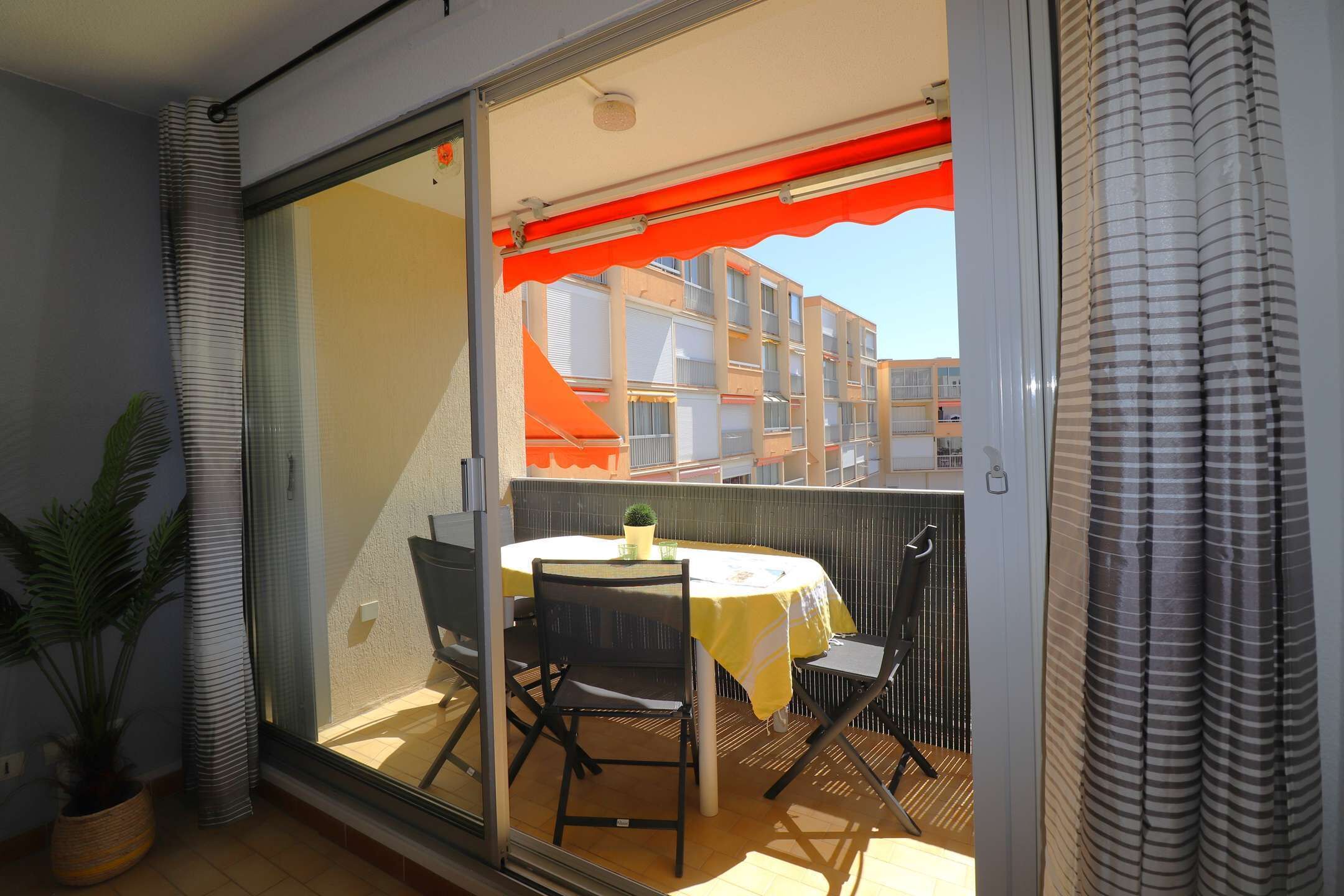 A balcony with a table and chairs, a potted plant, and a view of buildings.
