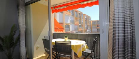 A balcony with a table and chairs, a potted plant, and a view of buildings.