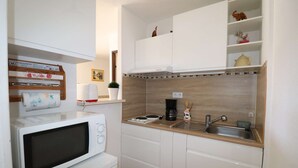 A compact kitchen with white cabinets, a microwave, a coffee maker, and a sink. - 2-room apartment for 4 people, 5 minutes from the beach (LE GRAU DU ROI)