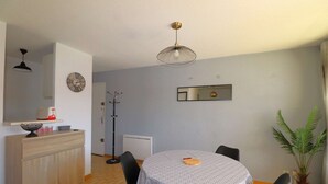 A dining area with a round table, chairs, a ceiling light, a wall clock, a radiator, and a potted plant. - 2-room apartment for 4 people, 5 minutes from the beach (LE GRAU DU ROI)