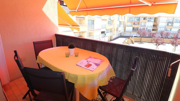 A balcony with a table and chairs, a potted plant, and a view of a building with balconies. - 2-room apartment for 4 people, 5 minutes from the beach (LE GRAU DU ROI)