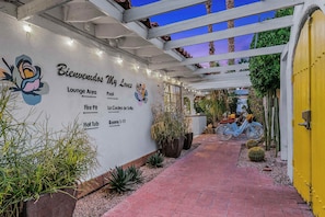 L’entrée d’un hôtel, avec un panneau indiquant un espace détente, un foyer extérieur et les chambres numérotées de 1 à 11.