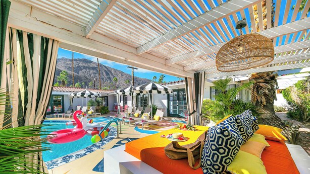 A poolside area with a lounge chair, a flamingo float, and a dining table with a drink. - Spirit of Sofia 12bd (Palm Springs)