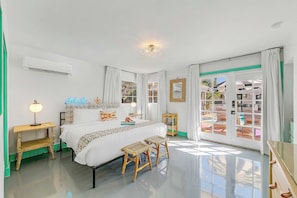 Une chambre à coucher avec un lit, des tables de chevet, une lampe, un miroir et une vue sur l’extérieur, visible à travers une porte vitrée.