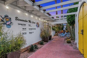 L’entrée d’un hôtel, avec un panneau indiquant un espace détente, un foyer extérieur et les chambres numérotées de 1 à 11.
