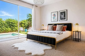 A bedroom with a large bed, a view of a swimming pool, and two framed artworks on the wall.
