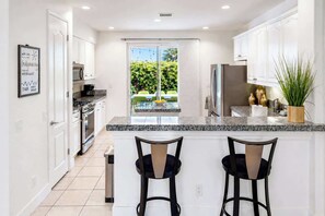 A modern kitchen with a large island, white cabinetry, and a view of greenery outside.