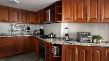 Uma cozinha com armários de madeira, bancadas de granito, forno embutido, cafeteira, liquidificador e torradeira.