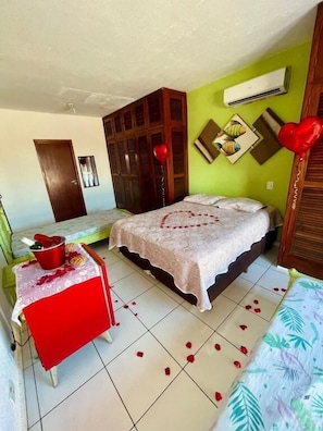 Quarto com cama, mesa com toalha vermelha, balão vermelho e ar-condicionado fixado na parede.