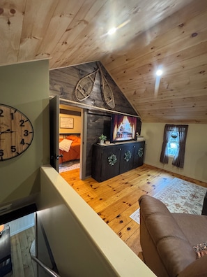A wooden interior with a clock, a fireplace, and a sofa.