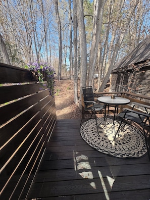 A wooden deck with a bench and a table with chairs, surrounded by trees.