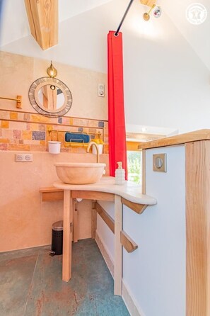 A compact bathroom with a wooden vanity, a large basin, a mirror, and a red curtain. - Un Temps Pour Soi - ANTULLY (ANTULLY)