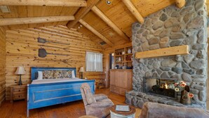 A log cabin bedroom with a stone fireplace, wooden furniture, and a bed with floral bedding. - Wilderness- Sedona Villas (Sedona)