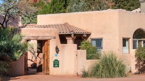 A building with a flat roof and a door, surrounded by desert vegetation and a large red rock formation. - Wilderness- Sedona Villas (Sedona)
