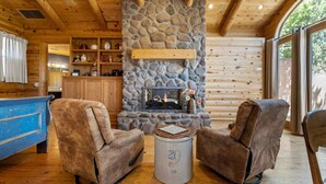 A cozy cabin interior with a stone fireplace, wooden furniture, and a view through large windows. - Wilderness- Sedona Villas (Sedona)