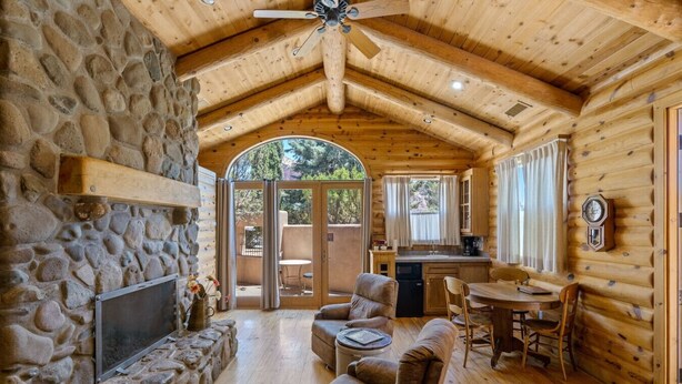 A log cabin interior with a stone fireplace, wooden ceiling, and a dining area. - Wilderness- Sedona Villas (Sedona)