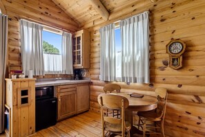 L’intérieur d’un chalet en bois comprend une cuisine, une table à manger, des chaises et une horloge au mur.