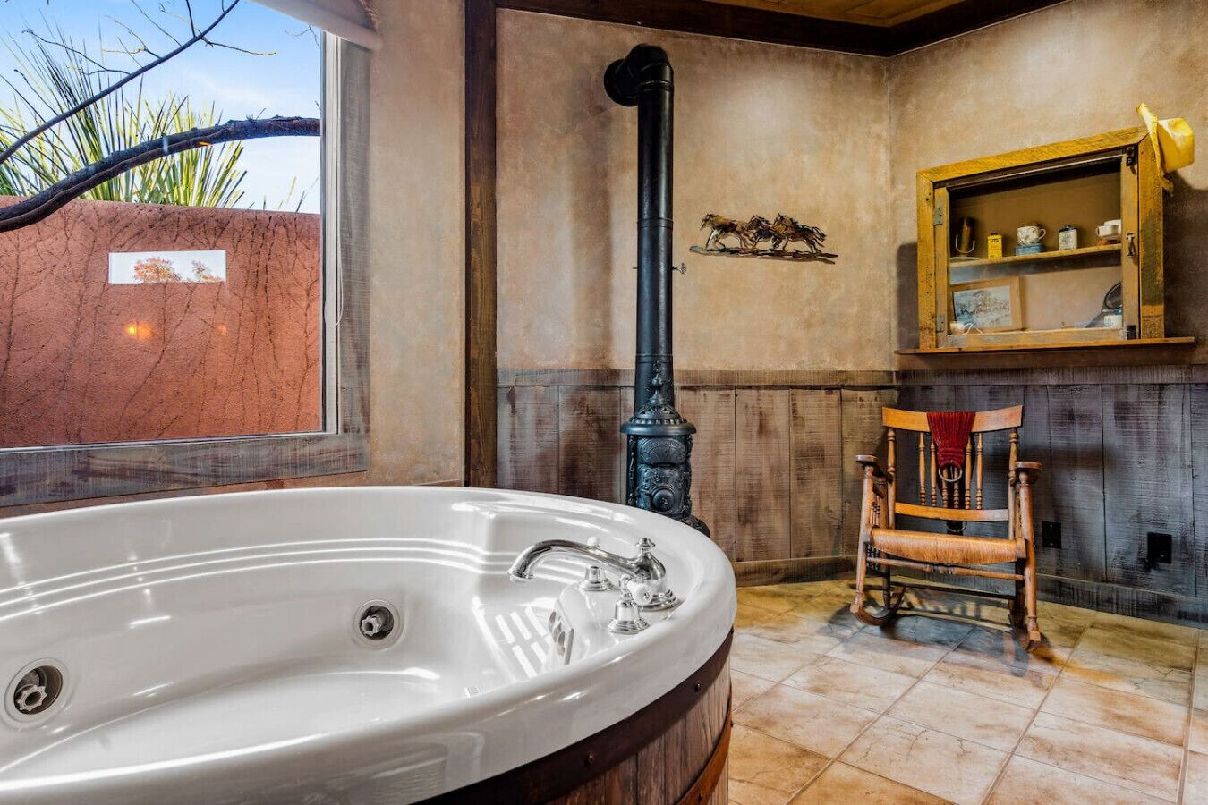 Un baño con una bañera grande, una silla de madera, una estufa antigua y una ventana con vistas a palmeras.