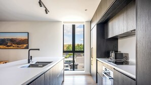 Une cuisine moderne dotée d’un grand îlot central, de meubles de rangement aux couleurs sombres et offrant une vue sur l’extérieur grâce à une porte vitrée.