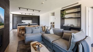 Un salon moderne avec un canapé d’angle, un coin repas et une cuisine en arrière-plan.